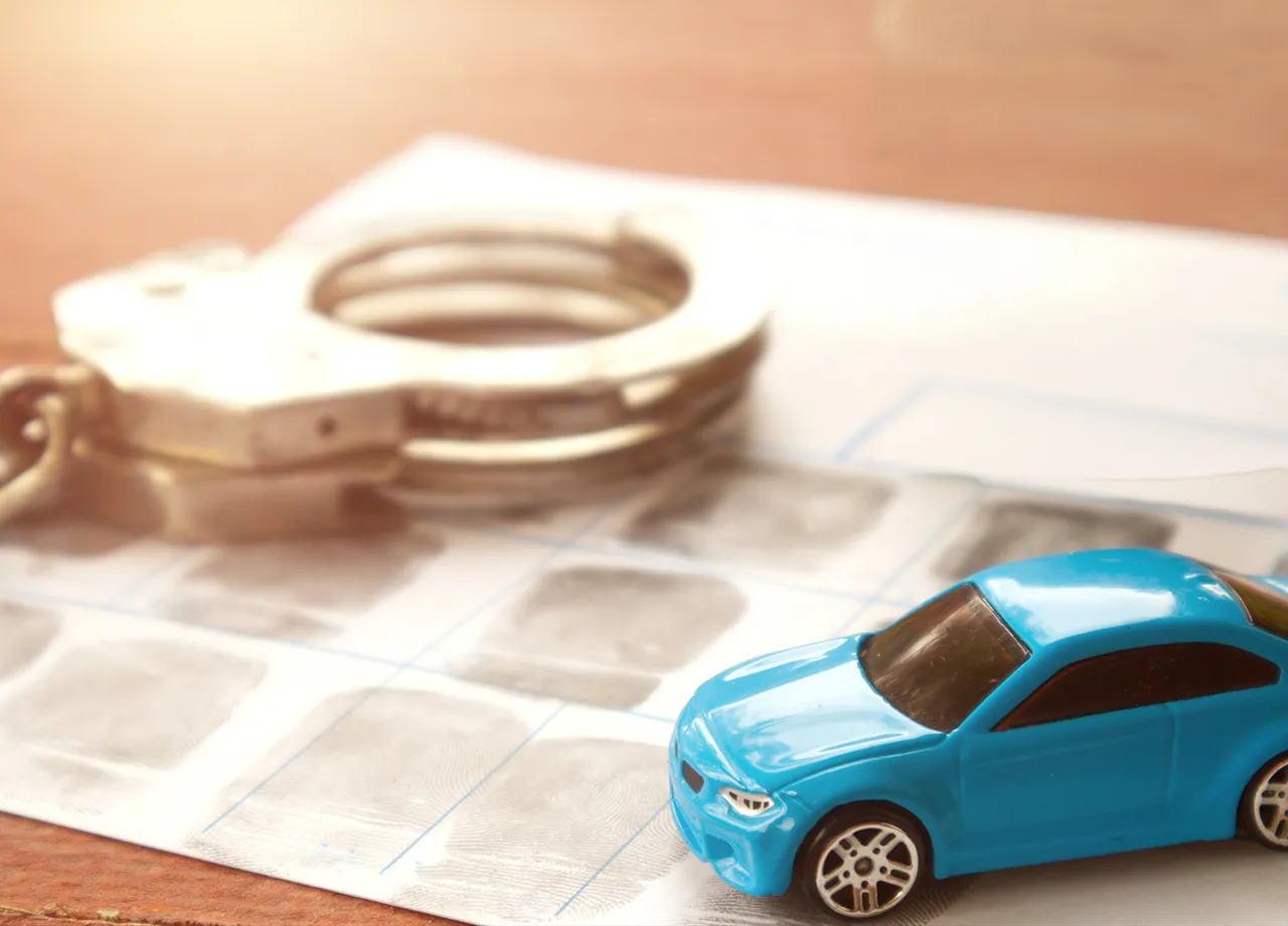 Ein Auto und Handschellen veranschaulichen eine Straftat im Straßenverkehr.