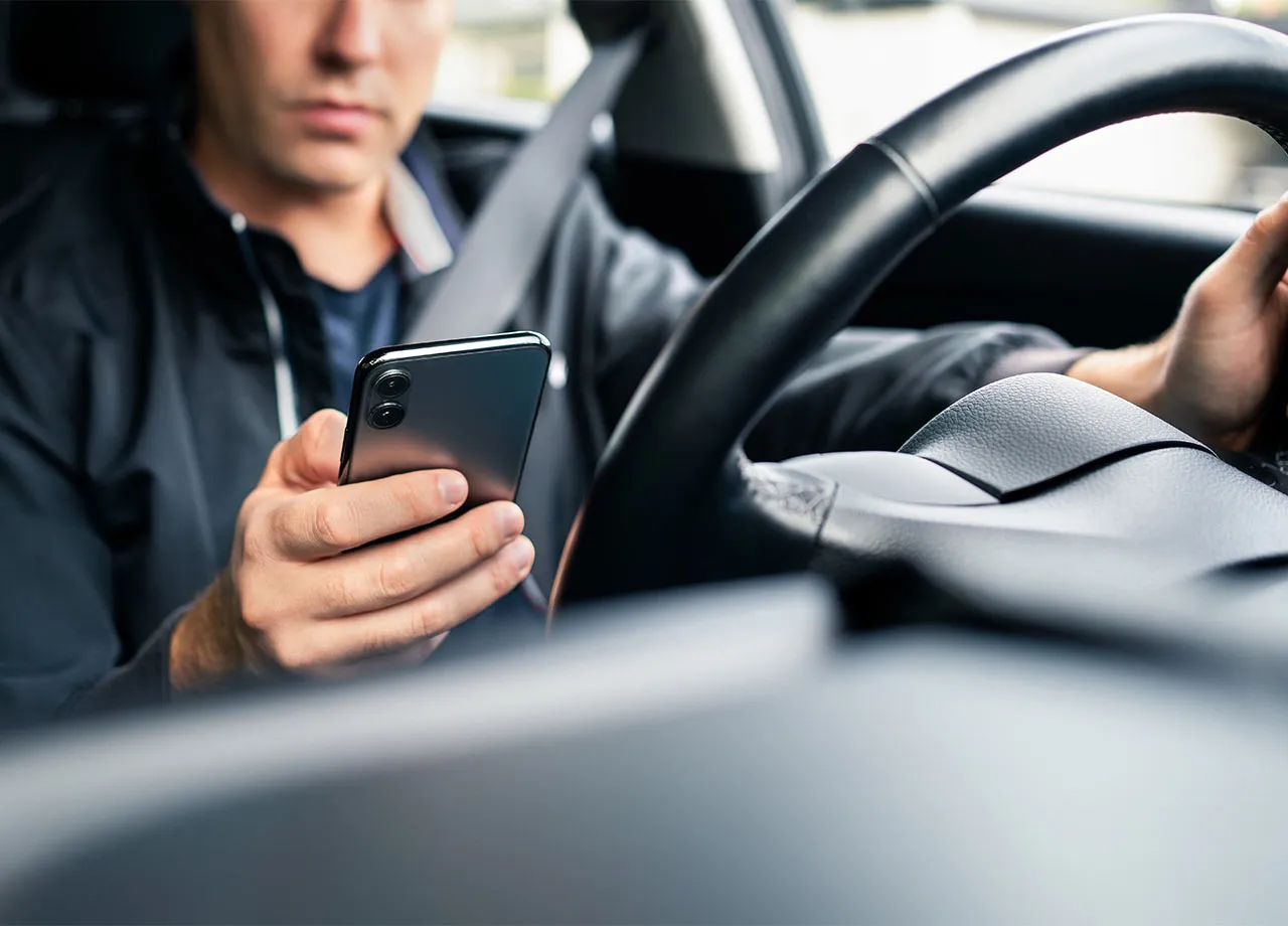 Ein Mann fährt mit dem Auto und hält dabei ein Handy in der Hand. Durch Monocam-Blitzer geblitzt.